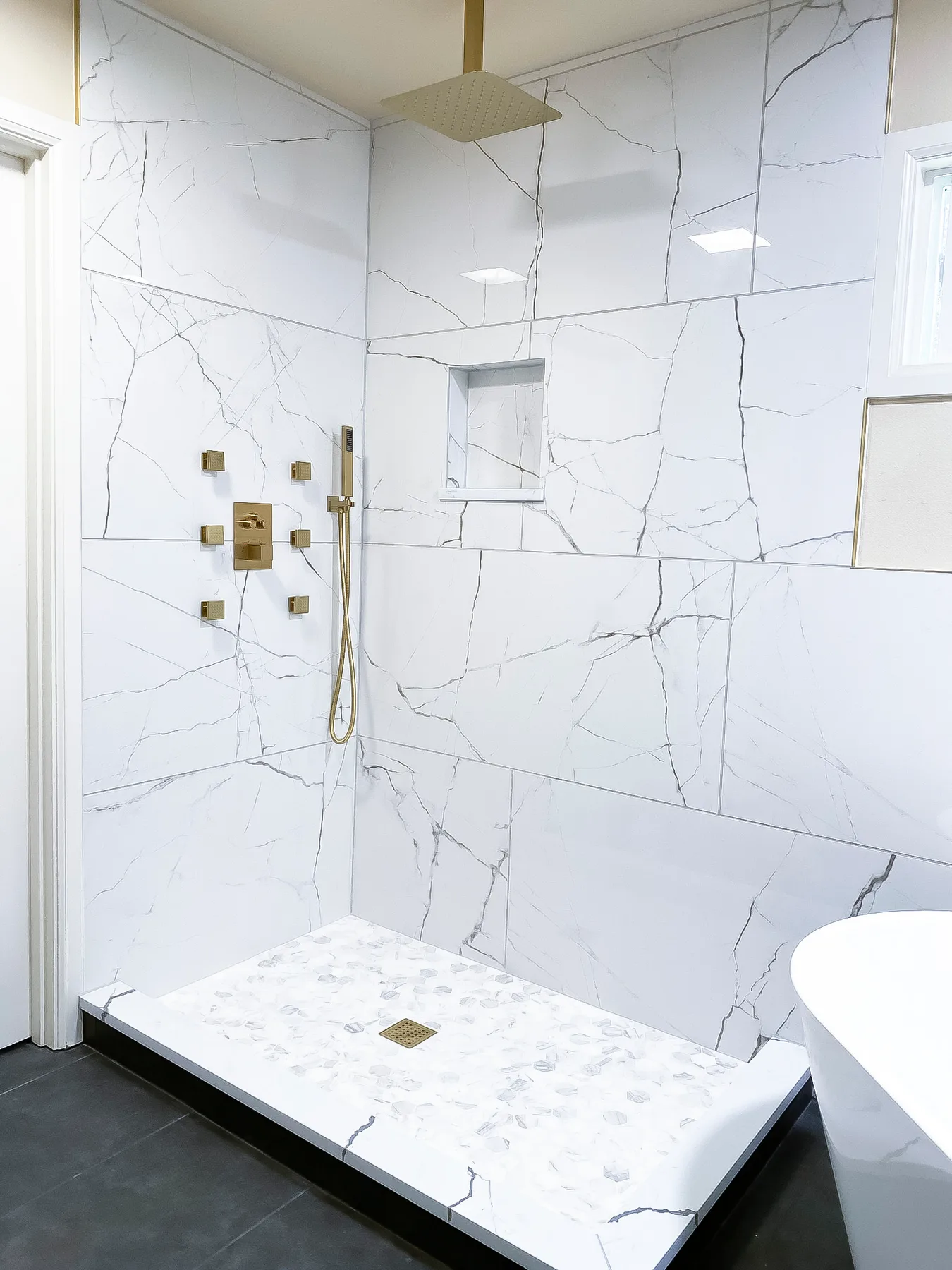 Finished marble-look shower with gold fixtures and freestanding tub in the remodeled primary bathroom in Issaquah, WA